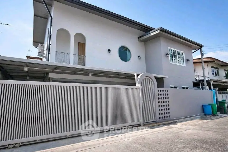 Modern two-story house with sleek design and gated entrance in a suburban neighborhood.