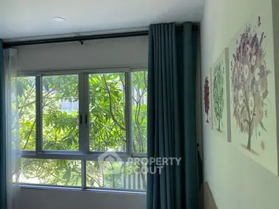 Bright bedroom with large window and lush garden view, featuring elegant wall art and dark curtains.