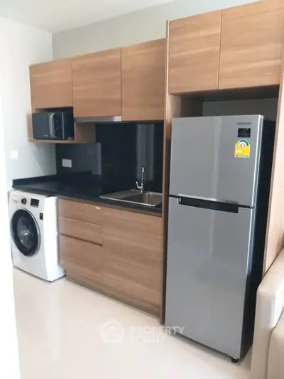 Modern kitchen with wooden cabinets, stainless steel fridge, and washing machine in sleek apartment.