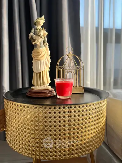 Elegant interior decor with woven side table, statue, and candle by sunlit window.