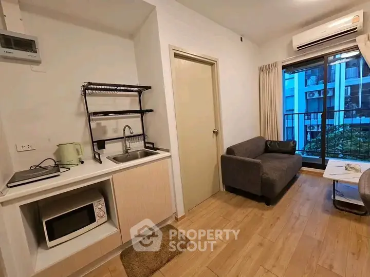 Cozy living room with modern kitchenette and balcony view in urban apartment.