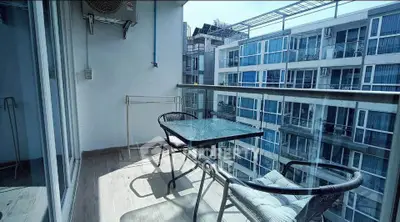 Modern balcony with glass railing and outdoor seating overlooking urban apartment complex.