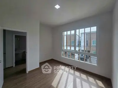 Bright empty room with large window and wooden flooring, perfect for customization.