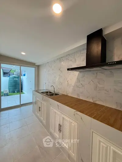 Modern kitchen with sleek countertops and stylish backsplash, featuring a sliding glass door to outdoor area.