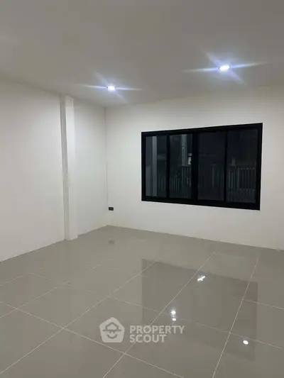 Spacious empty room with glossy tiled floor and large window, perfect for customization.