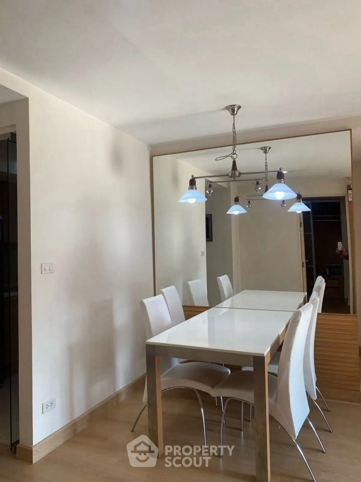 Modern dining area with sleek white chairs and elegant lighting in a stylish apartment.