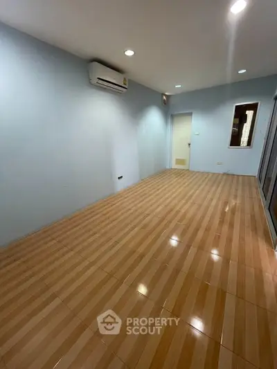 Spacious empty room with wooden flooring and air conditioning, ideal for customization.