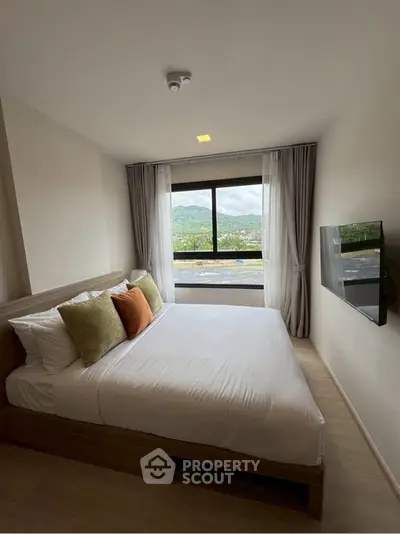 Modern bedroom with scenic mountain view from large window, featuring a cozy bed and wall-mounted TV.