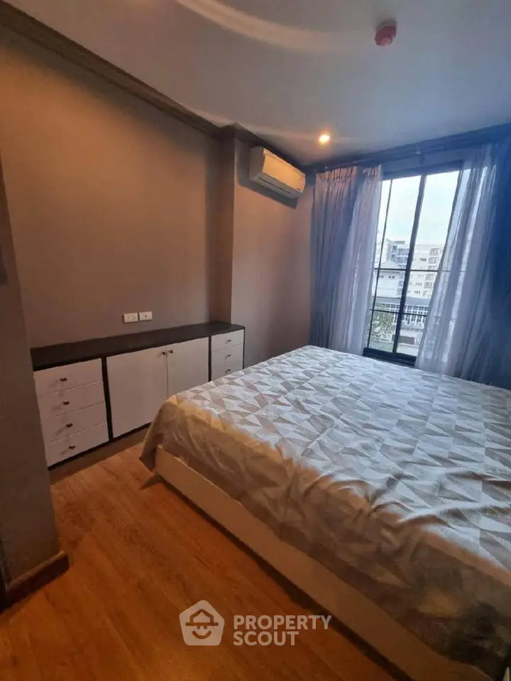 Cozy bedroom with modern decor and large window offering city views, featuring a comfortable bed and ample storage.