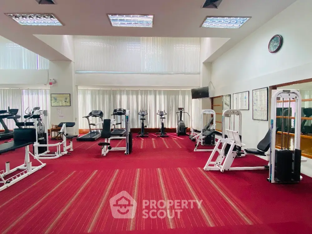 Spacious gym with modern equipment and vibrant red carpet, perfect for fitness enthusiasts.