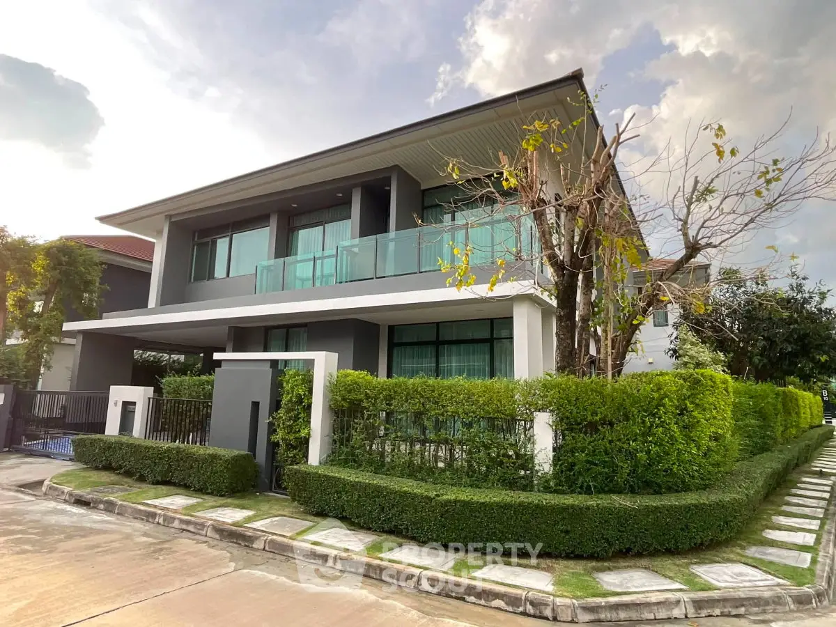 Modern two-story house with lush greenery and sleek glass balcony in a serene neighborhood.