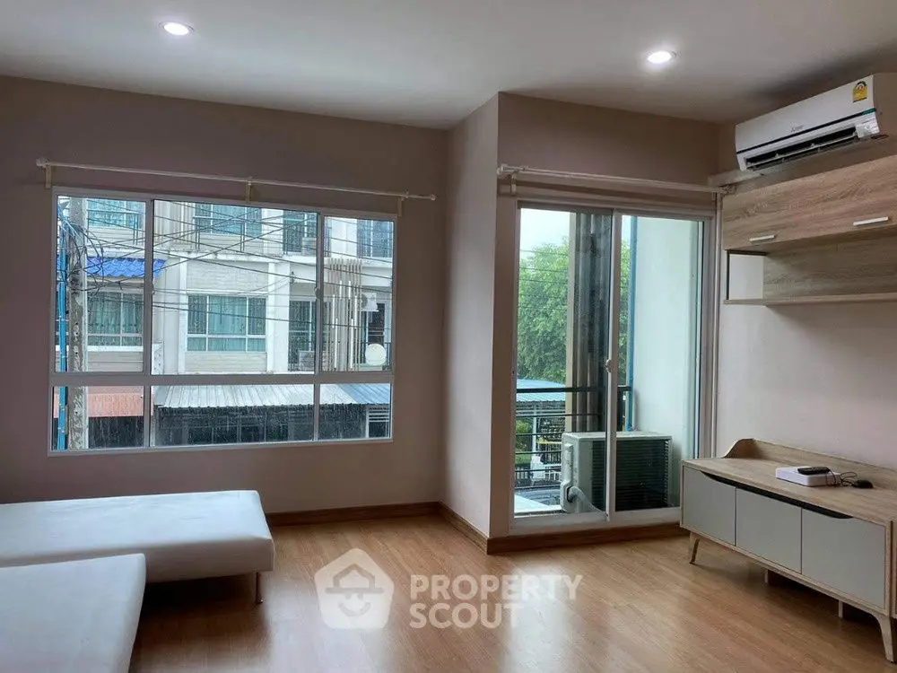 Modern living room with large windows and air conditioning, featuring wooden flooring and minimalist furniture.