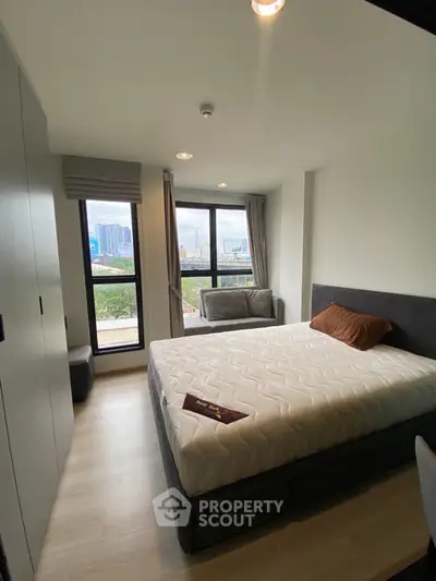 Modern bedroom with large windows and city view, featuring a comfortable bed and stylish decor.