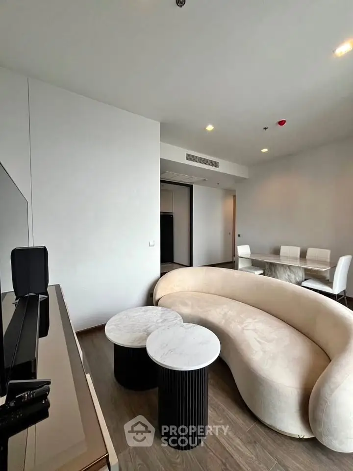 Modern living room with elegant curved sofa and chic dining area in open layout apartment.
