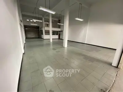 Spacious industrial-style interior with high ceilings and tiled flooring, ideal for commercial use.