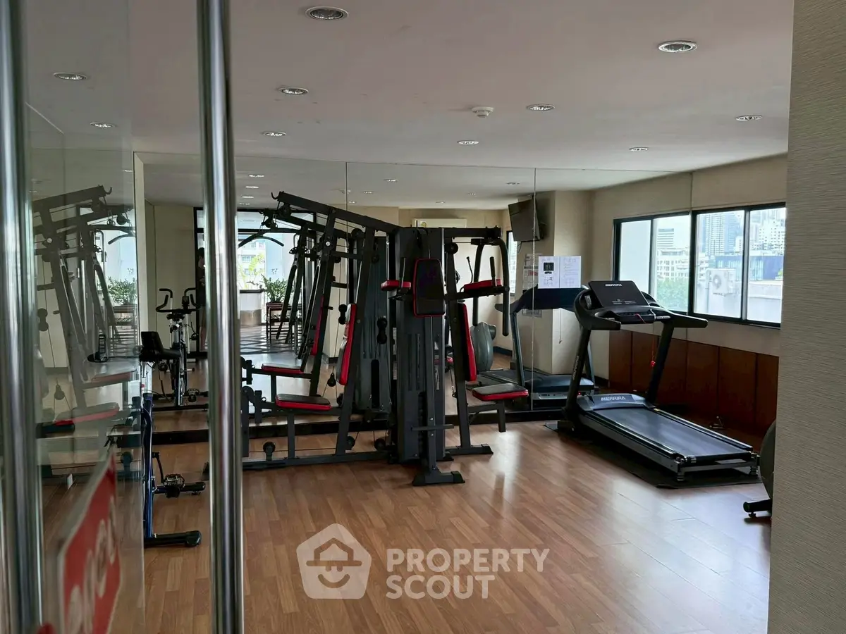 Spacious gym with modern equipment and mirrored walls in a high-rise building.