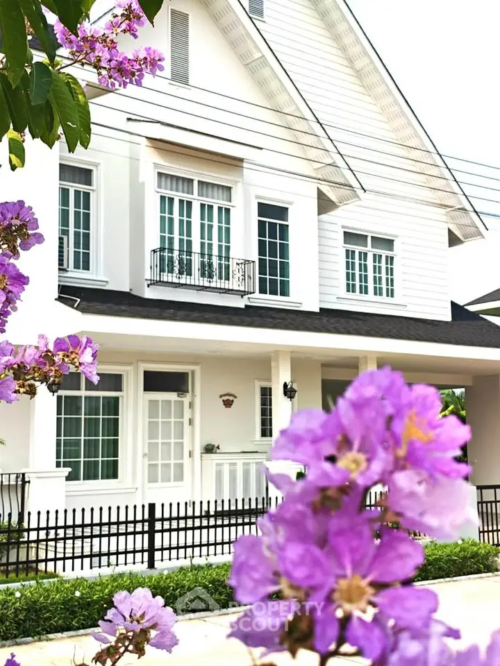 Charming white house with purple flowers, featuring classic architecture and a welcoming front porch.
