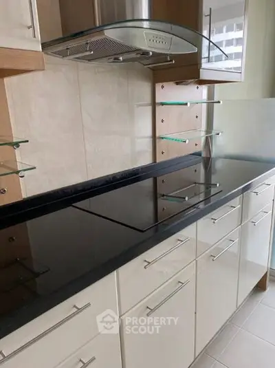Modern kitchen with sleek black countertop and glass shelves, featuring a built-in electric stove.