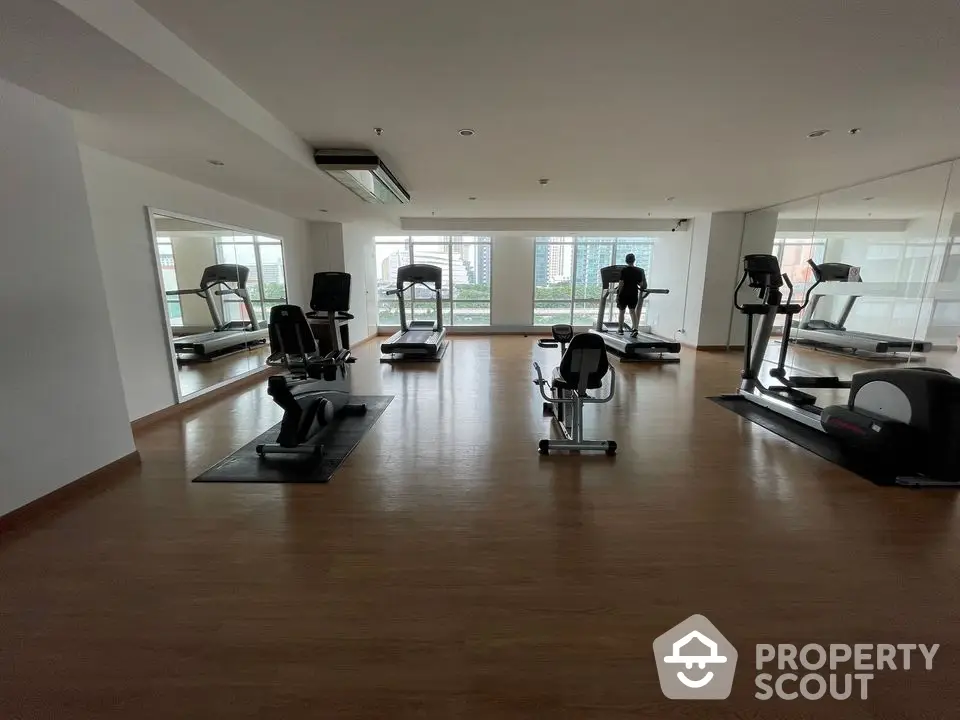 Spacious gym with modern equipment and city view in luxury apartment complex