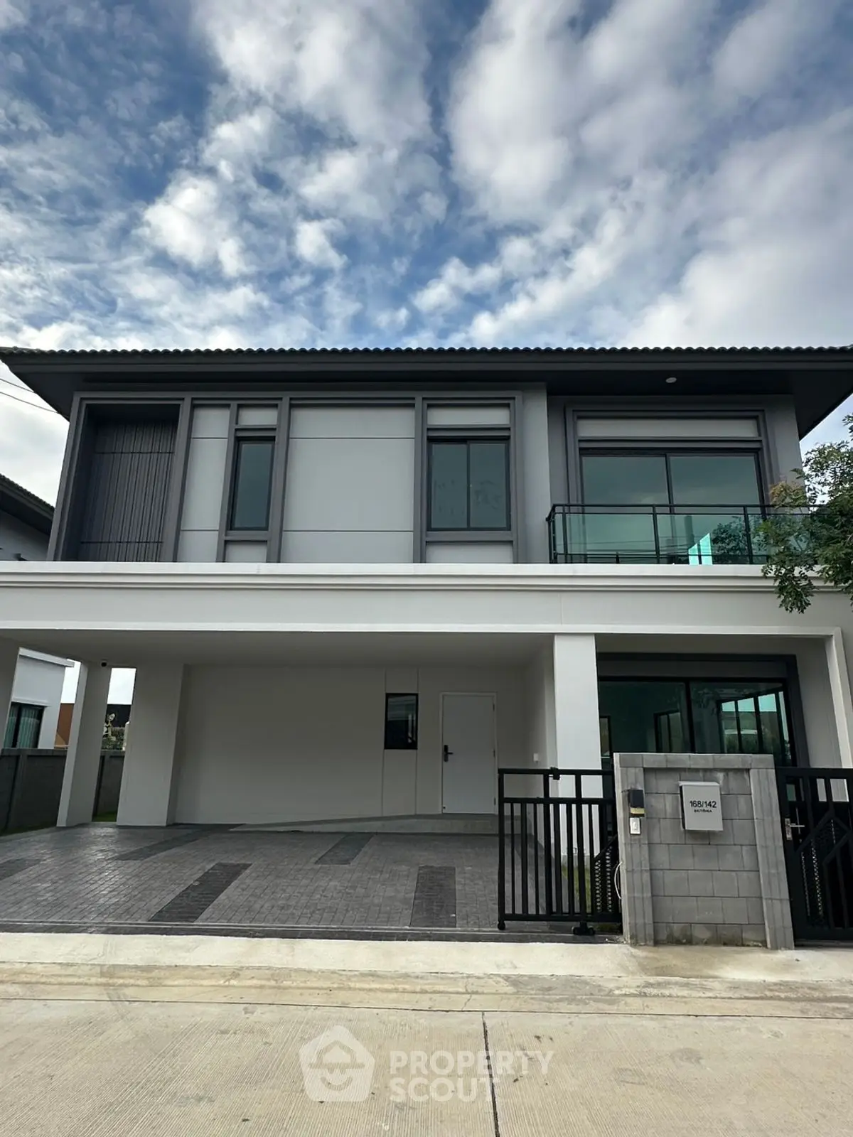 Modern two-story house with sleek design and spacious driveway under a cloudy sky.