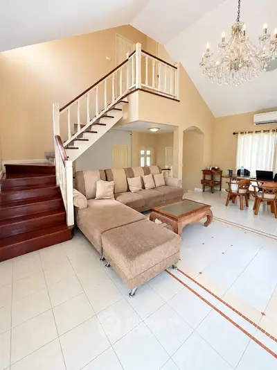 Spacious living room with elegant staircase and chandelier, perfect for family gatherings.