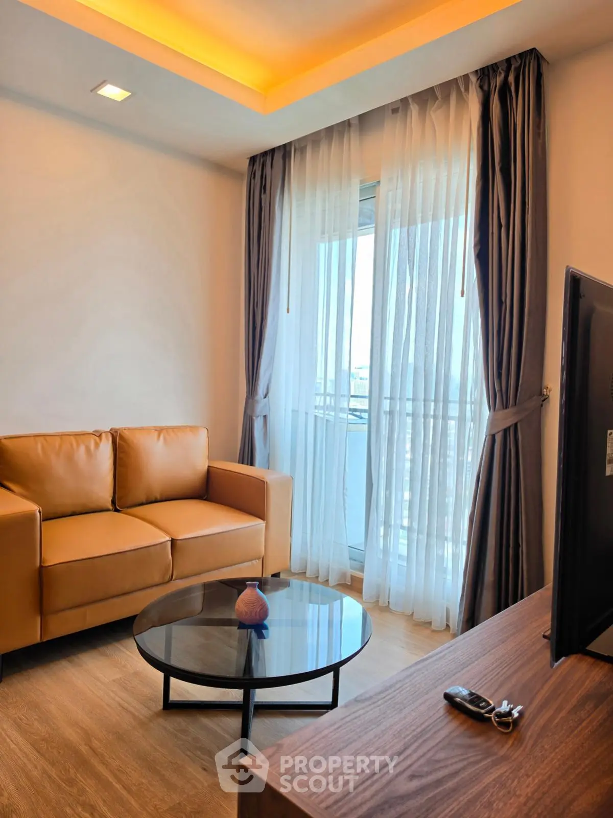 Modern living room with leather sofa, glass coffee table, and large window with city view.