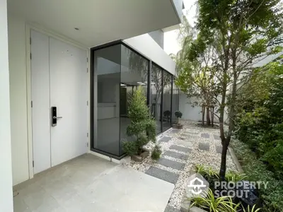 Modern entrance with sleek glass walls and lush garden path