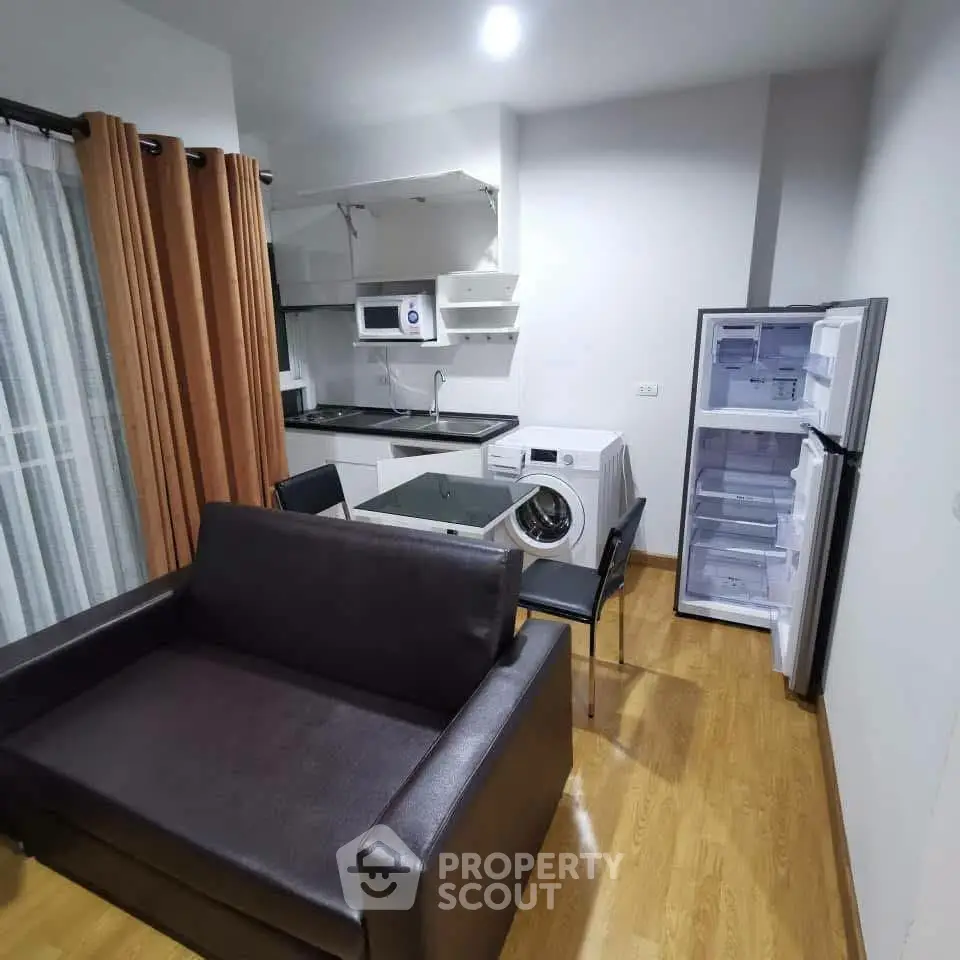 Modern compact living room with kitchen, featuring sofa, dining table, washing machine, fridge, and microwave.