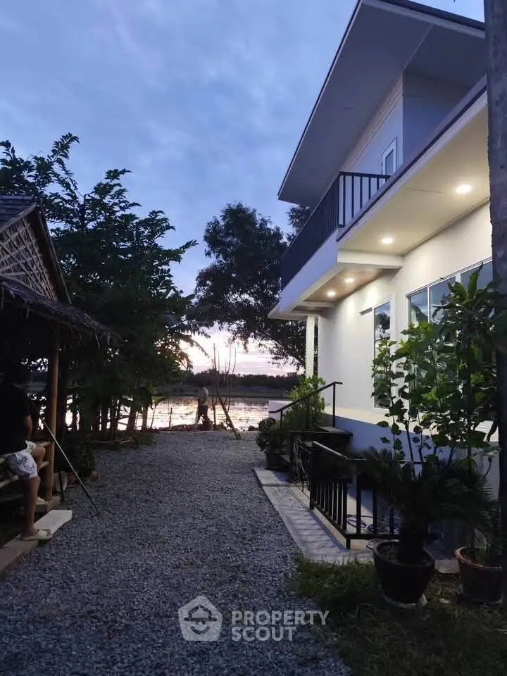 Modern two-story house with balcony and garden by the lakeside at dusk, offering serene views.