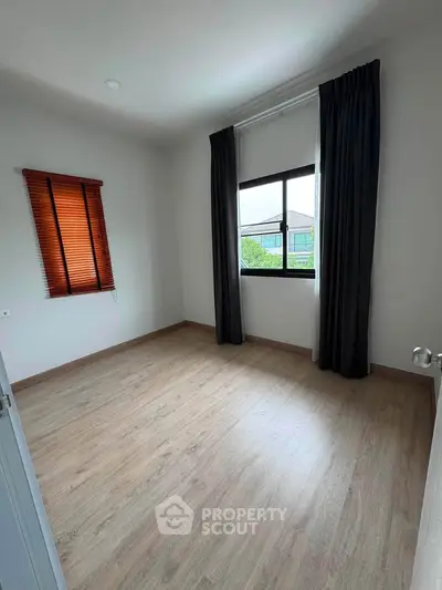 Spacious empty bedroom with large window and wooden flooring, perfect for customization.