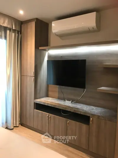 Modern living room with sleek wooden entertainment unit and mounted TV, featuring elegant lighting and air conditioning.