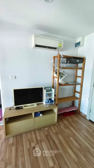 Modern living room with air conditioning and wooden flooring, featuring a TV and shelving unit.