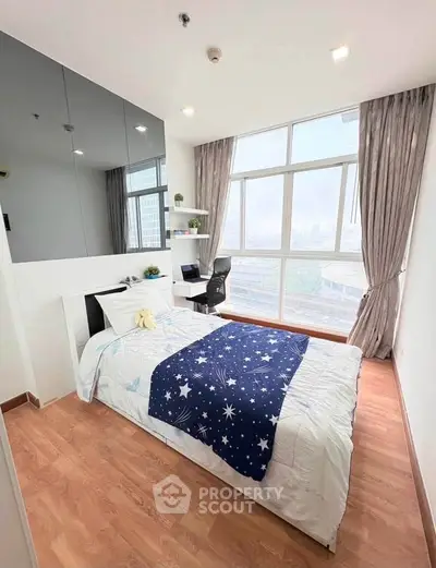 Bright bedroom with large windows and city view, featuring a cozy bed and study area.