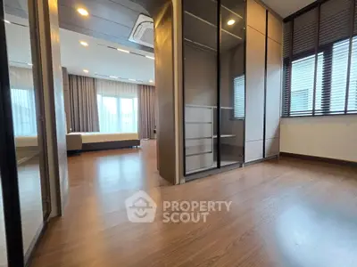 Spacious modern bedroom with wooden flooring and large windows for natural light.