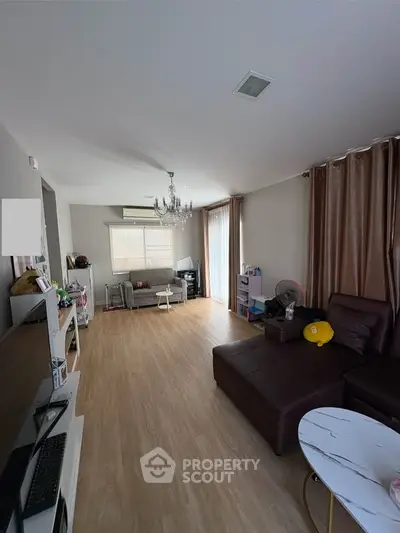 Spacious living room with modern decor and wooden flooring, featuring a cozy seating area and elegant chandelier.