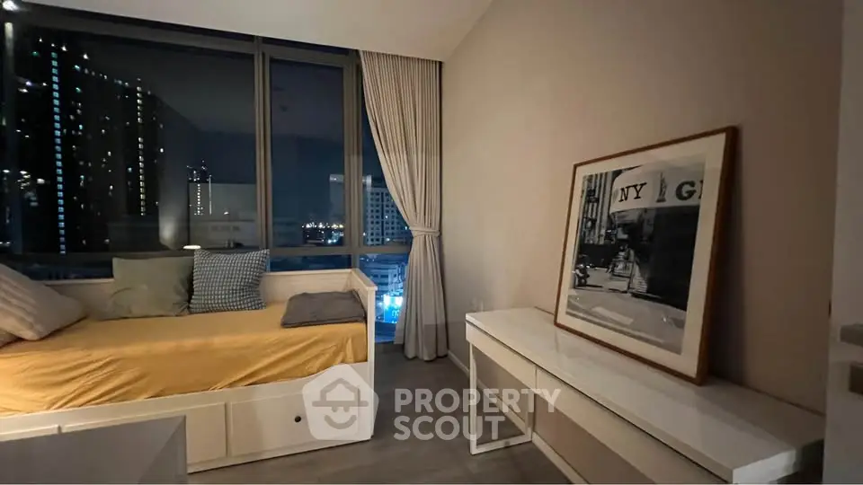 Cozy modern bedroom with city view, featuring stylish decor and large windows for natural light.