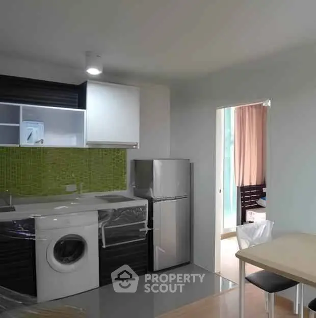 Modern kitchen with green backsplash, washing machine, and compact fridge in stylish apartment.