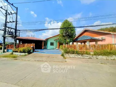 Charming single-story home with terracotta roof tiles and a spacious front yard, featuring a cozy porch and a vibrant wooden fence, set against a clear blue sky.