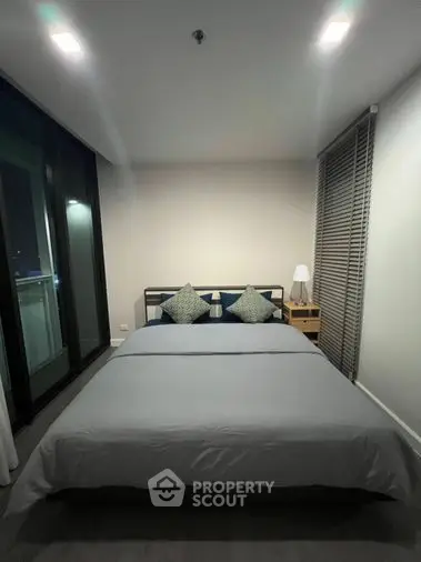 Sleek modern bedroom with a large comfortable bed, stylish lighting, and a sliding glass door leading to a balcony, offering a serene urban living experience.