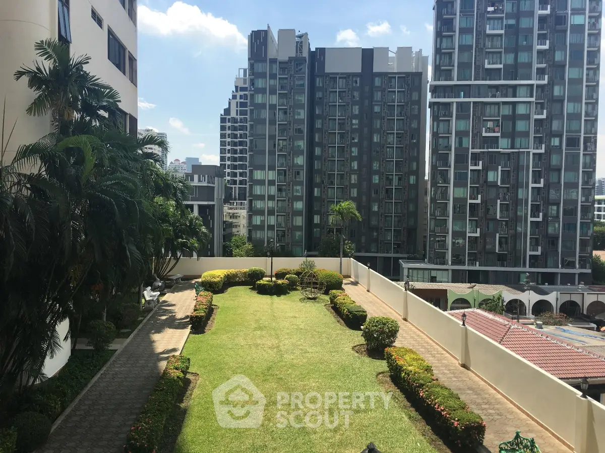 Spacious garden area in modern apartment complex with lush greenery and city views.