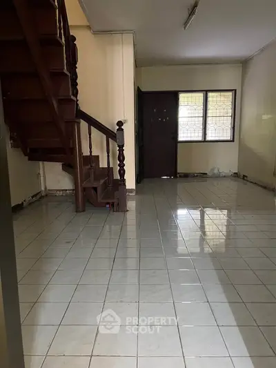 Spacious interior with tiled flooring and wooden staircase, ideal for renovation.