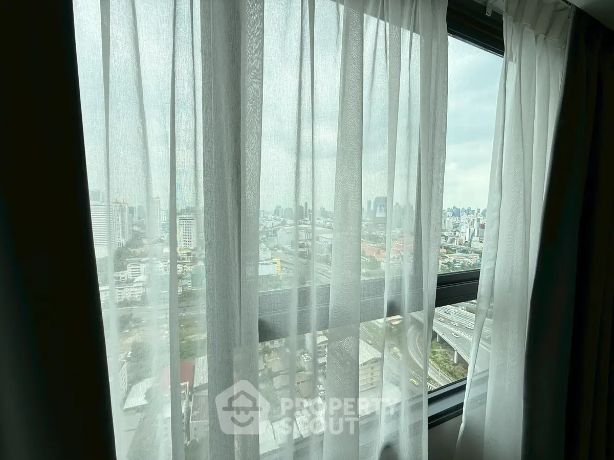 Stunning cityscape view through sheer curtains from a high-rise apartment window.