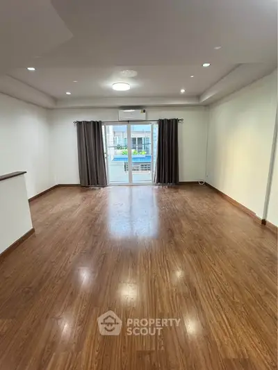 Spacious living room with wooden flooring and large windows offering natural light.