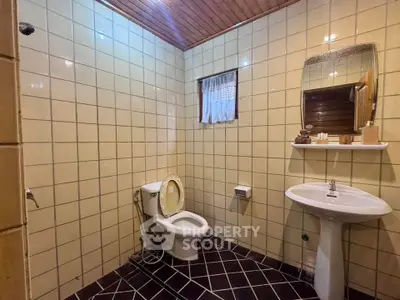 Cozy bathroom with tiled walls and wooden ceiling, featuring a toilet and pedestal sink.