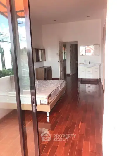 Spacious bedroom with wooden flooring and large windows for natural light.