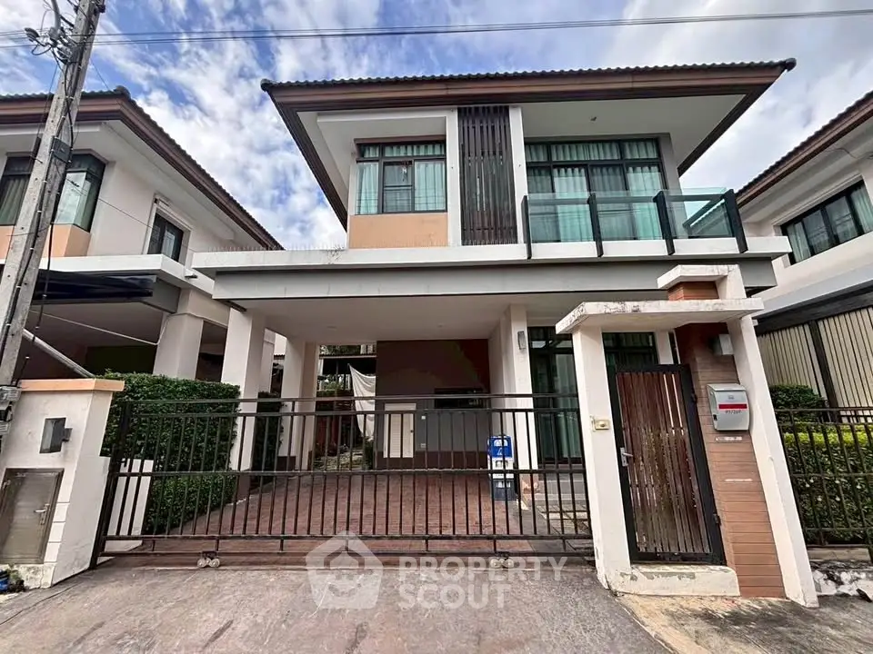 Modern two-story house with gated driveway and large windows in a suburban neighborhood.