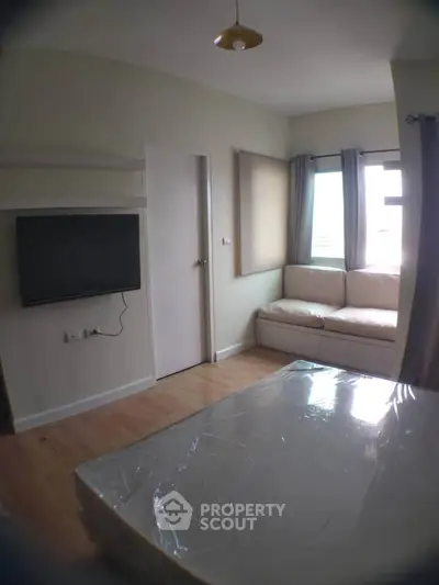 Cozy bedroom with natural light, featuring a wall-mounted TV and a comfortable seating area by the window.