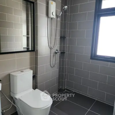 Modern bathroom with sleek tiles and shower, featuring a large window for natural light.