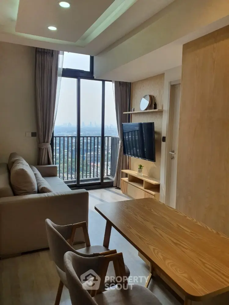 Cozy living room with modern furniture, large windows offering a stunning city view, and access to a spacious balcony, perfect for urban living.