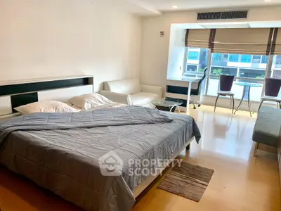 Spacious bedroom with modern furnishings and natural light, featuring a cozy seating area and work desk.